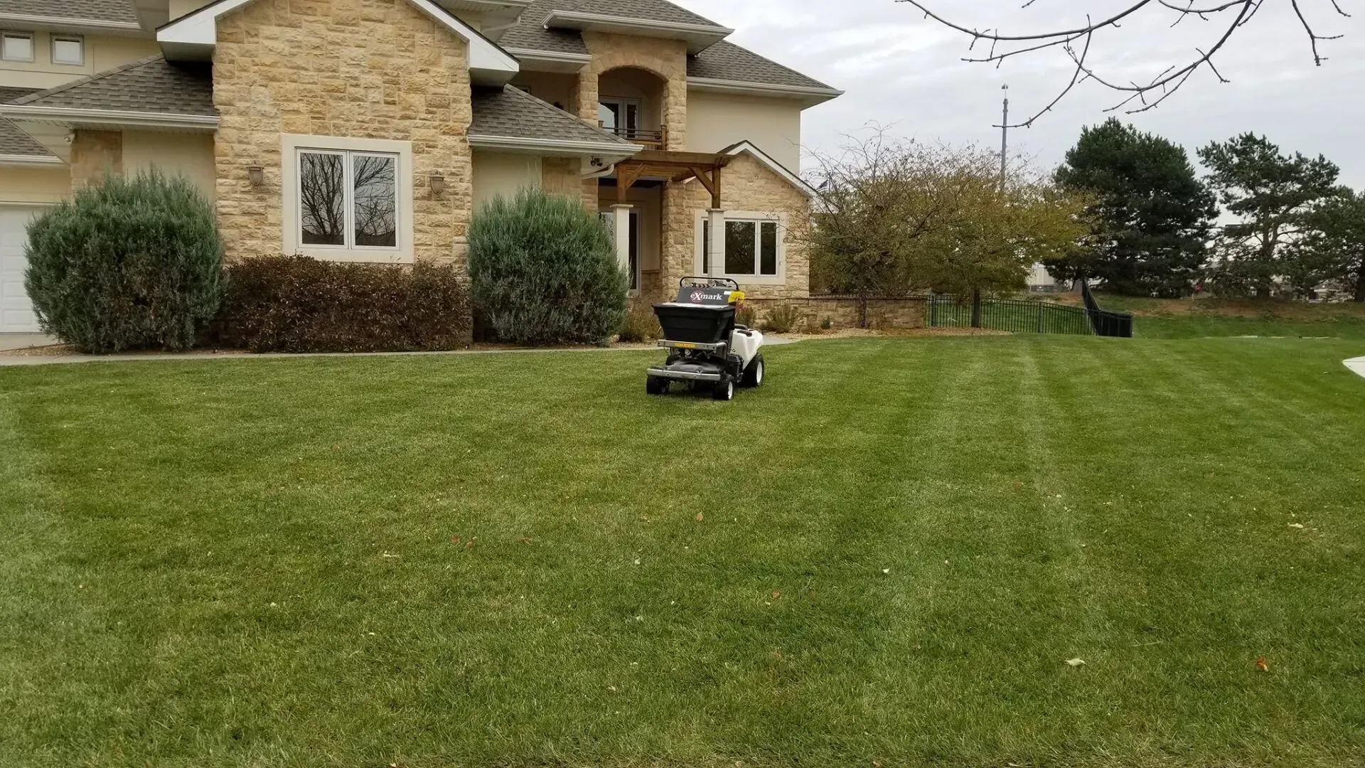 A lawn mower is cutting a lush green lawn in front of a large house.
