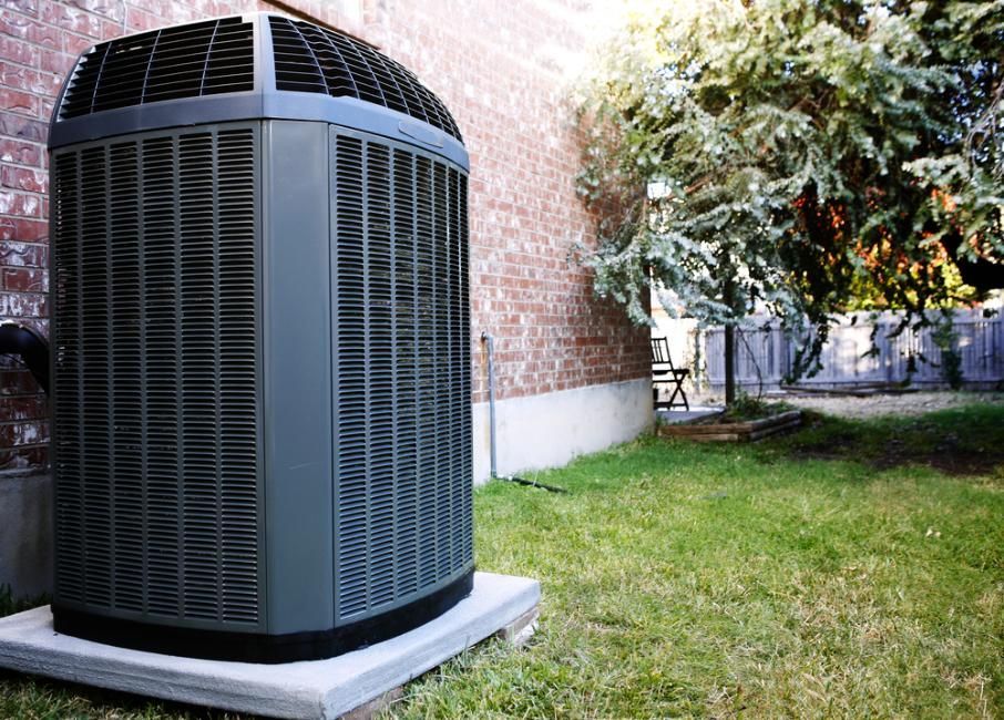A Large Air Conditioner is Sitting in the Grass in Front of a Brick Building — AJM's Air Conditioning Centre in Wardell, NSW