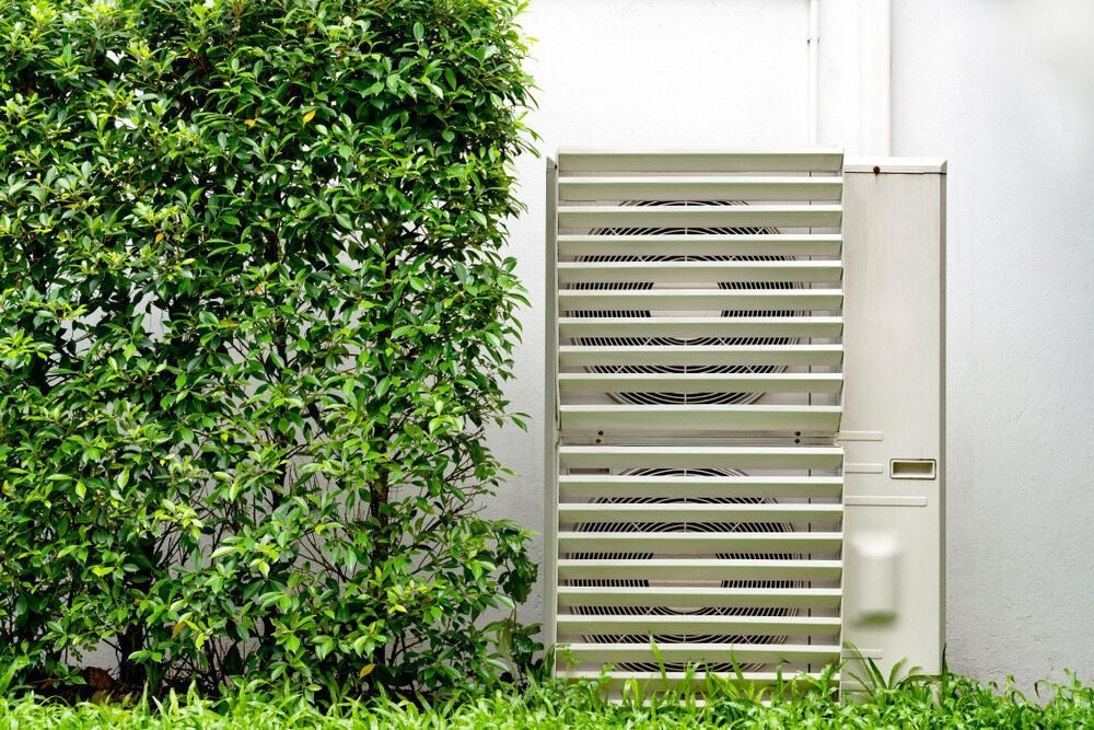 A White Air Conditioner is Sitting on the Side of a Building Next to a Bush — AJM's Air Conditioning Centre in Lismore, NSW