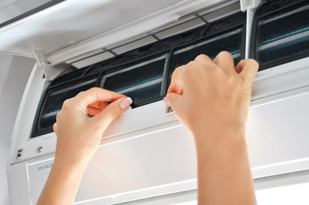 A Person is Cleaning an Air Conditioner With a Screwdriver — AJM's Air Conditioning Centre in Alstonville, NSW