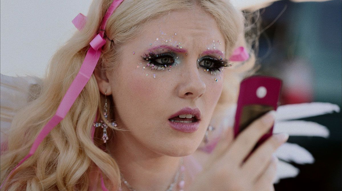 A woman dressed as a barbie doll is looking at her phone.