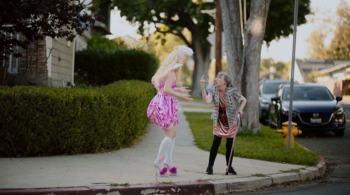 A woman in a pink dress is standing next to a girl in a pink dress on a sidewalk.