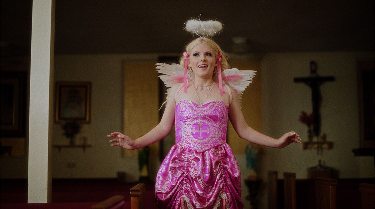 A woman in a pink dress and angel wings is standing in a church.