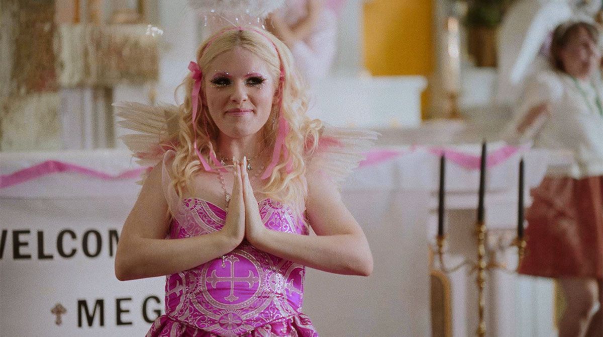 A woman in a pink dress and pink hair is praying in a church.