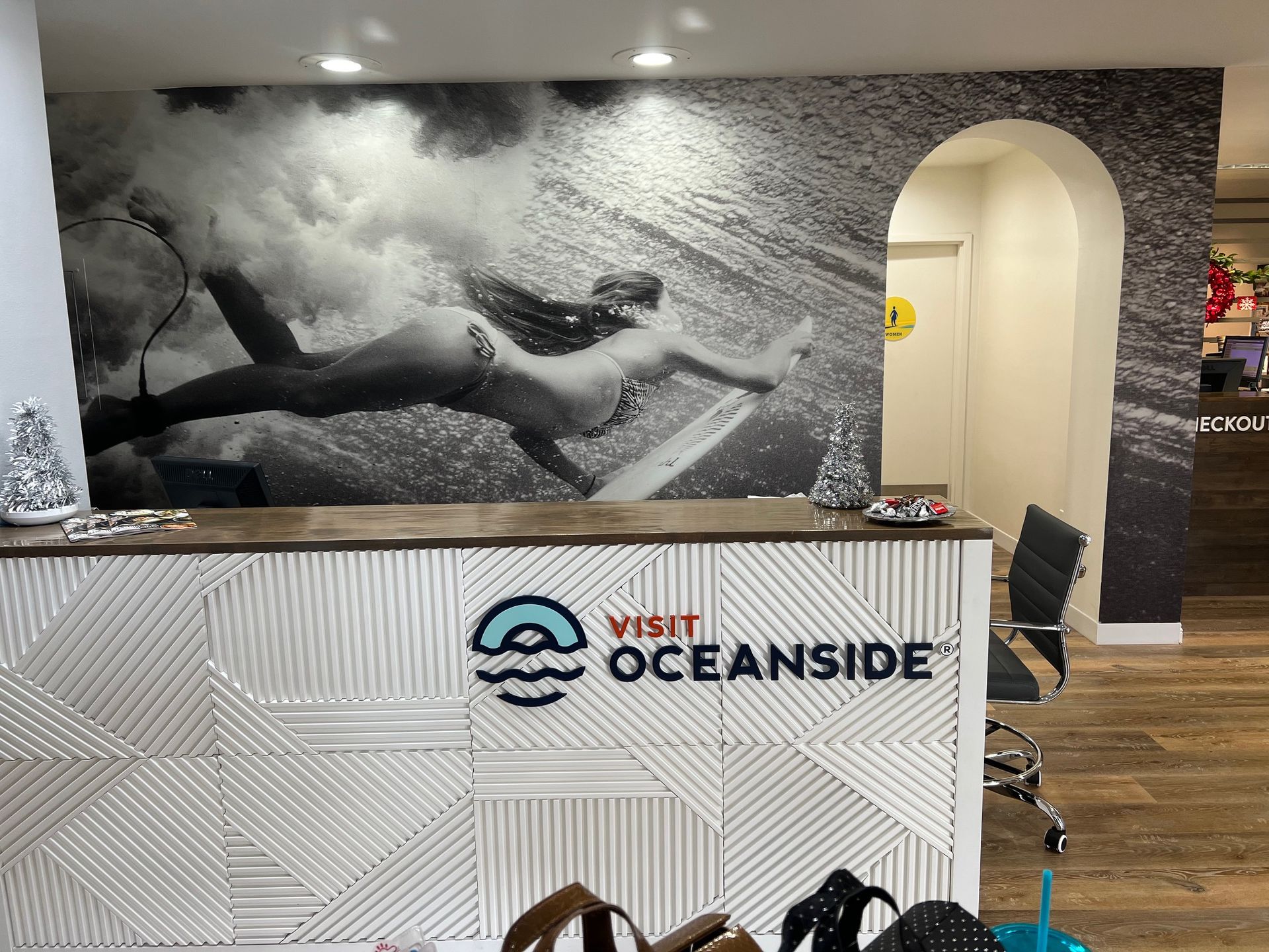 Visit Oceanside reception desk with black-and-white surfer mural and arched hallway.