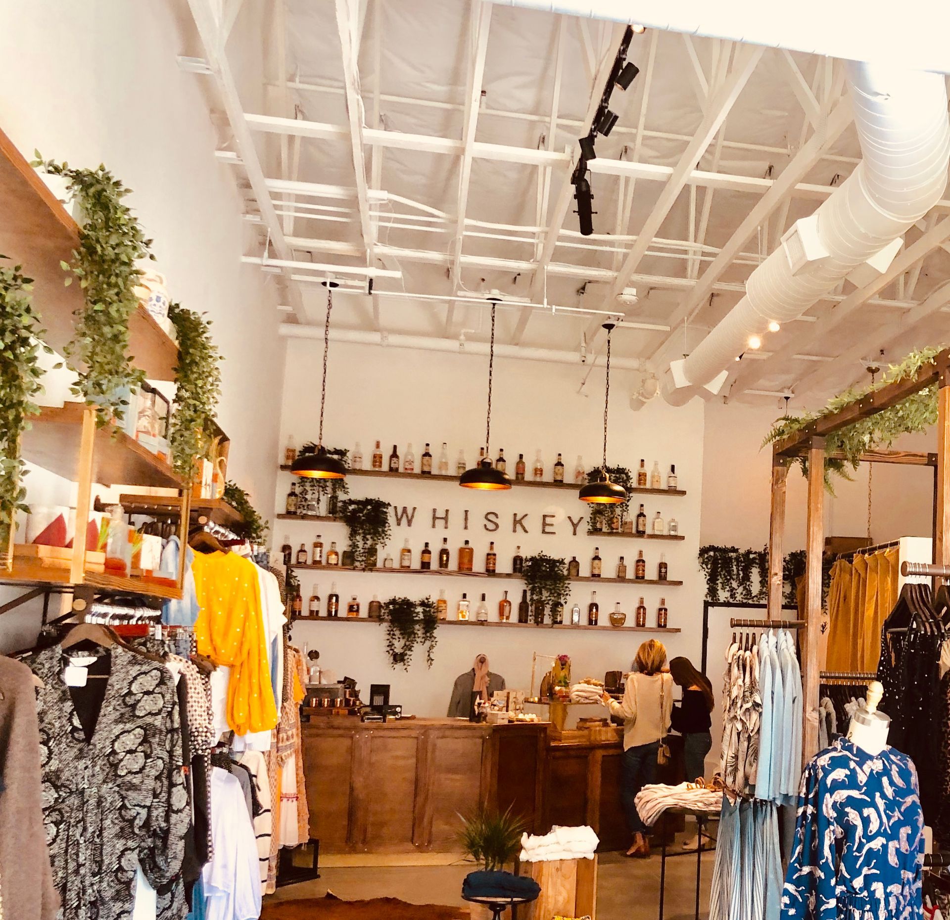 Clothing boutique with wooden shelves, hanging garments, and a whiskey bar display at the back