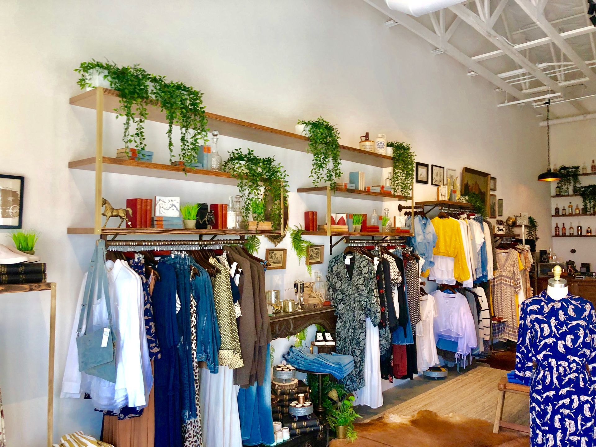 Boutique clothing store with racks of colorful garments and wall shelves with plants and decor