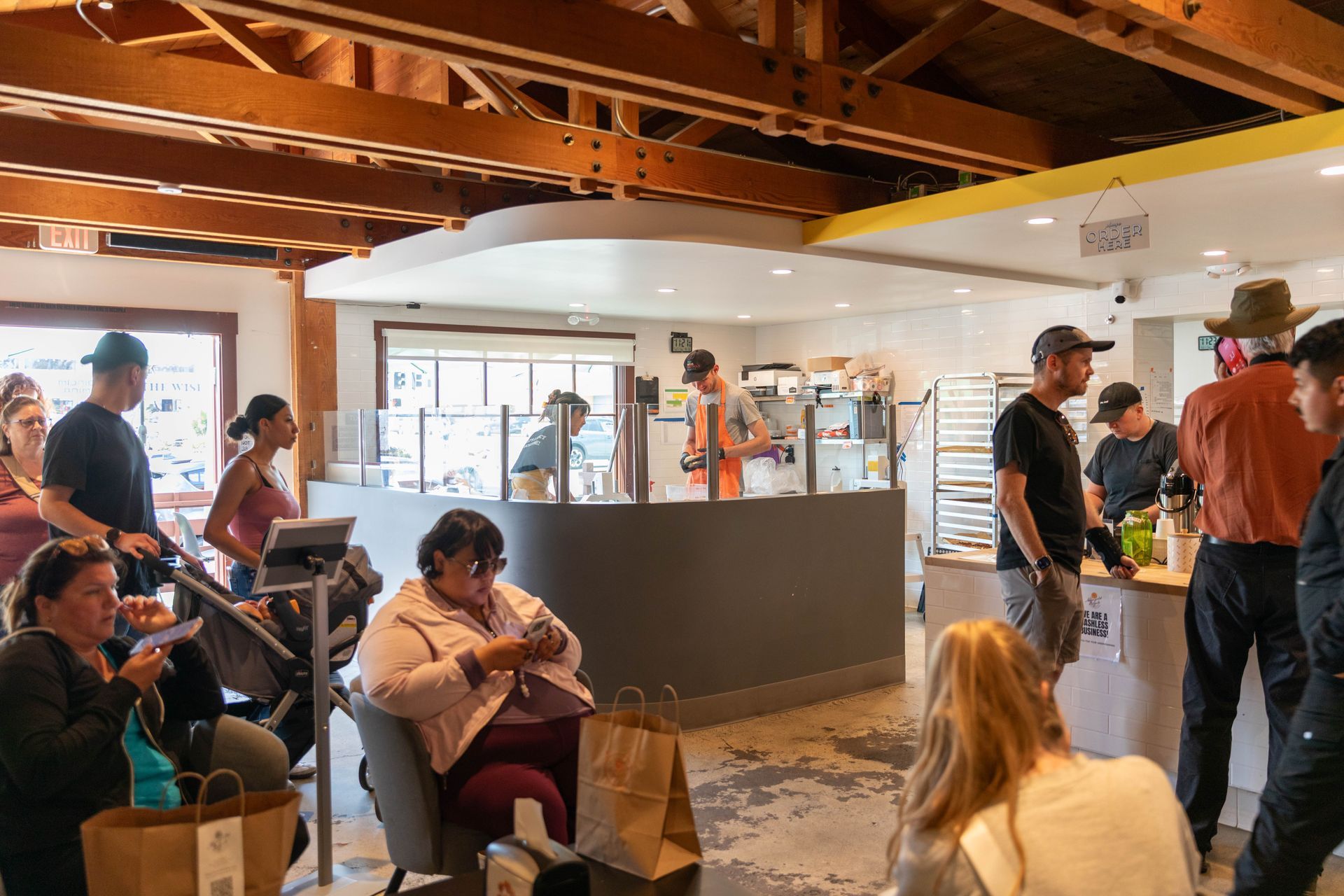 People seated and standing in a busy indoor café or event space with exposed wooden beams.