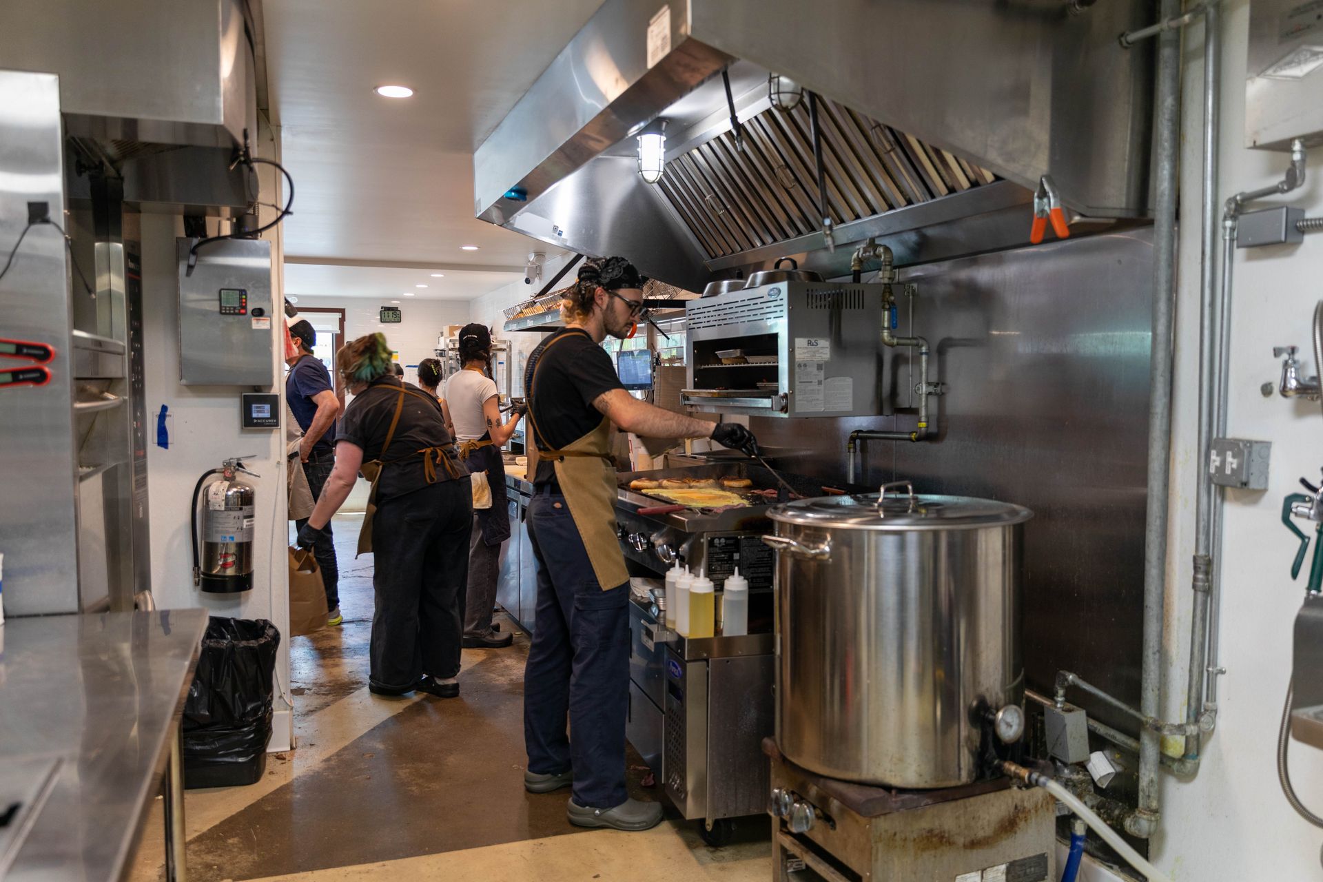 Chefs working in a stainless steel commercial kitchen with large pots and exhaust hood