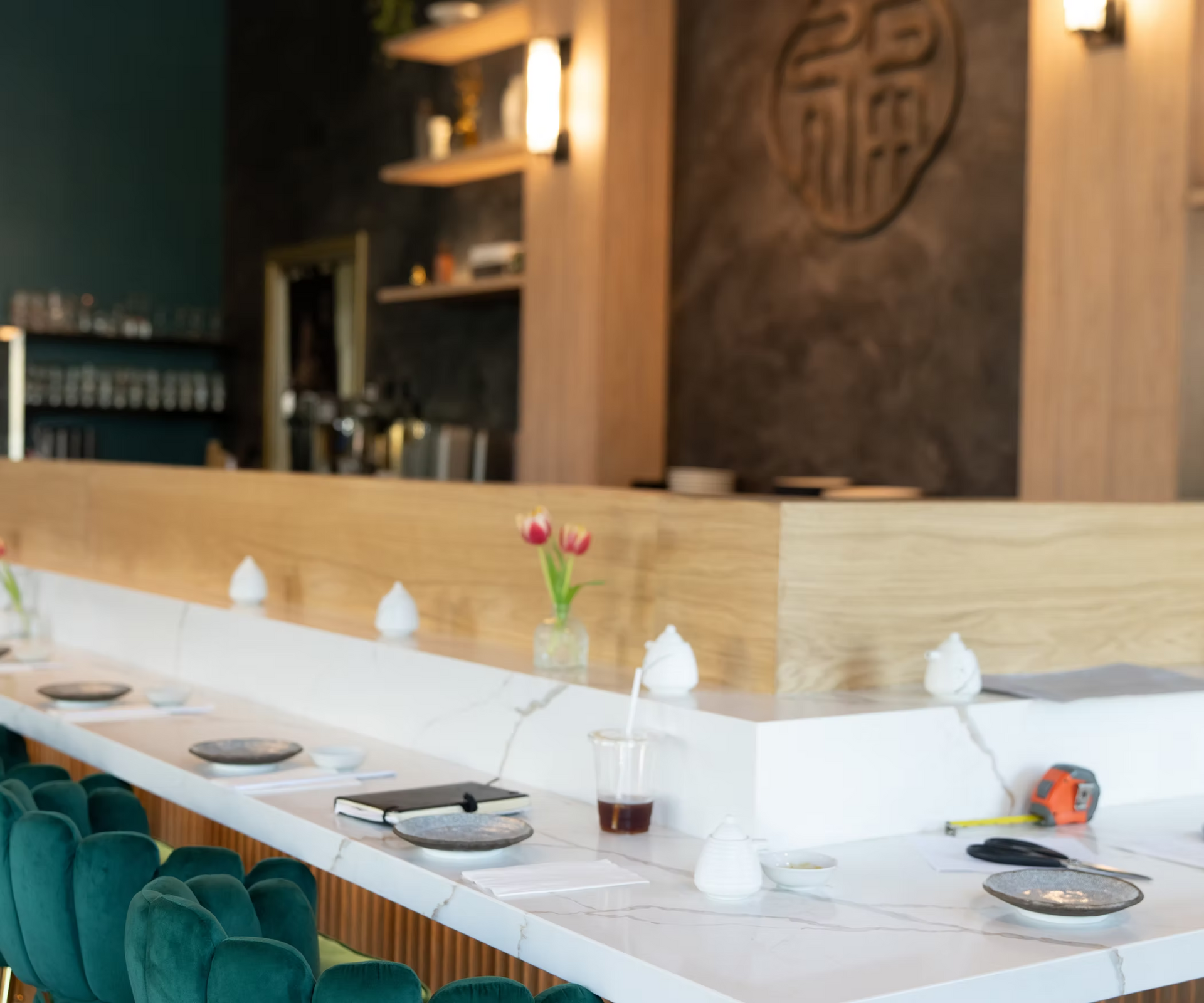 Empty sushi bar counter with white table settings and a small flower vase in a warm wood interior