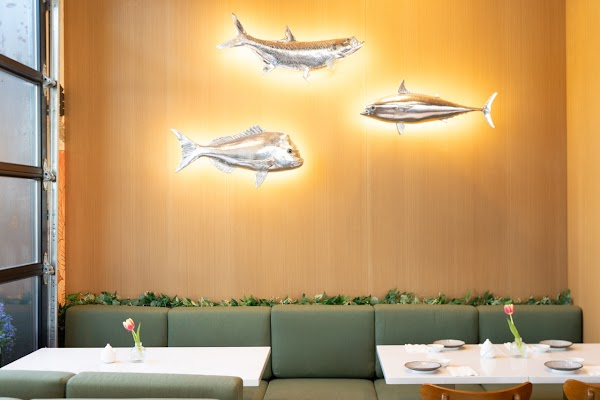 Modern restaurant interior with green banquette seating, white tables, and illuminated fish wall sculptures.