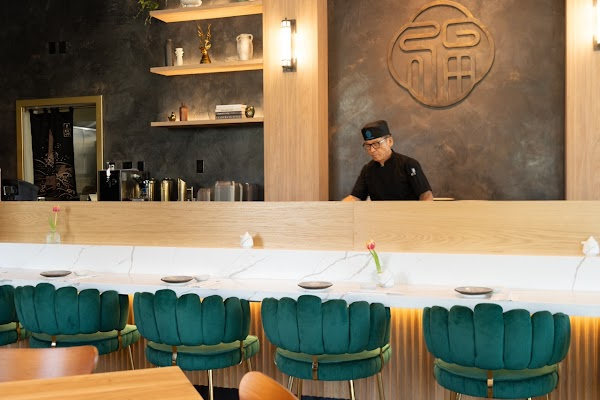 Modern café bar interior with teal stools, wood counter, shelves, and a barista behind the counter