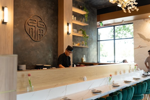Modern restaurant interior with a chef behind a long wooden counter and large window seating area