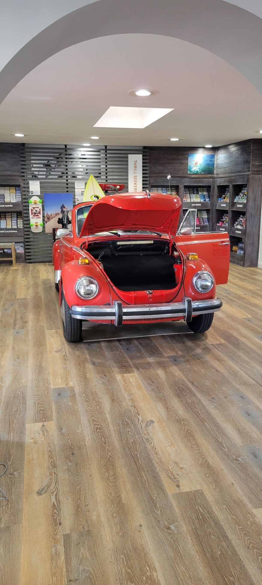 Red classic car with hood open displayed in an indoor showroom under an arched ceiling.
