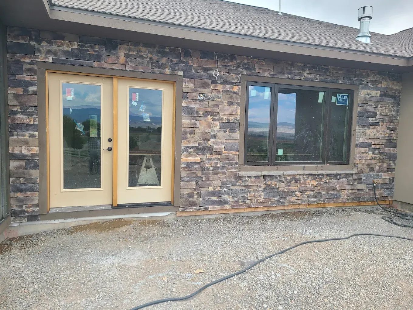 Stone-clad exterior with glass doors and window, light brown trim, gravel patio.