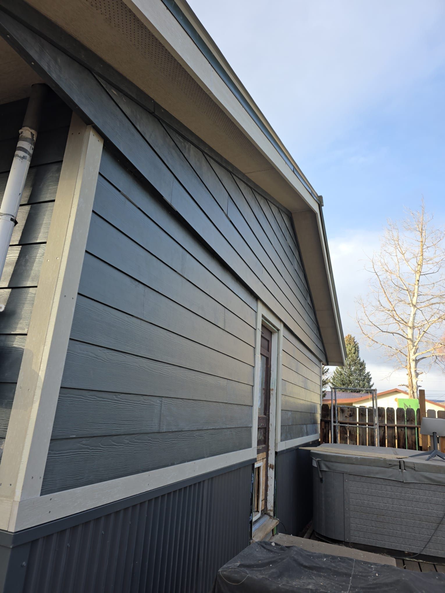 Blue-sided house exterior with white trim, an open doorway, and a partly cloudy sky.