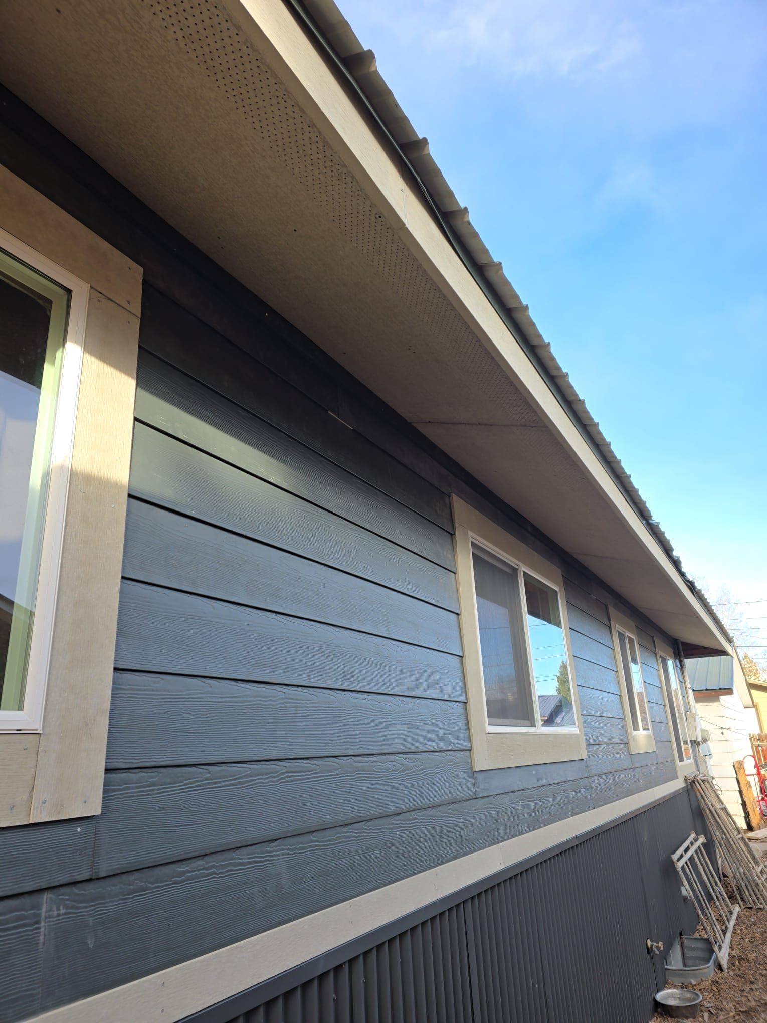 Blue-sided house with beige trim and windows. A blue sky is in the background.