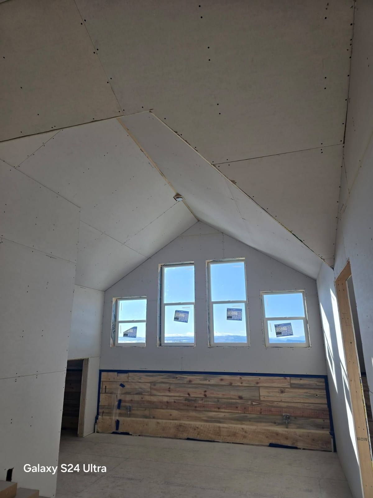 Interior of a room under construction, featuring drywall, windows, and a wooden accent wall.