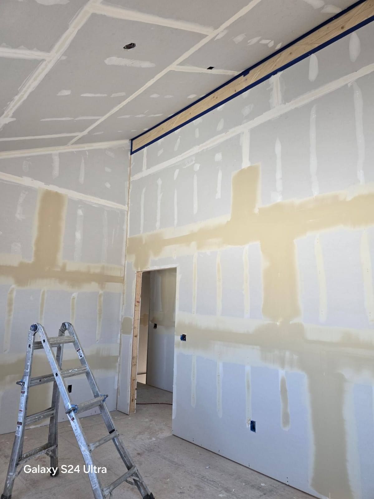 Interior room with drywall installation in progress; ladder, taped edges, and mudding visible.