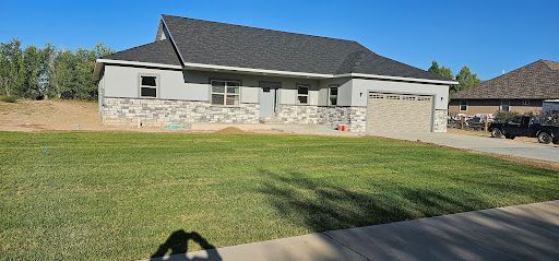 A light gray house with a dark gray roof. A lawn in the foreground with a blue sky.