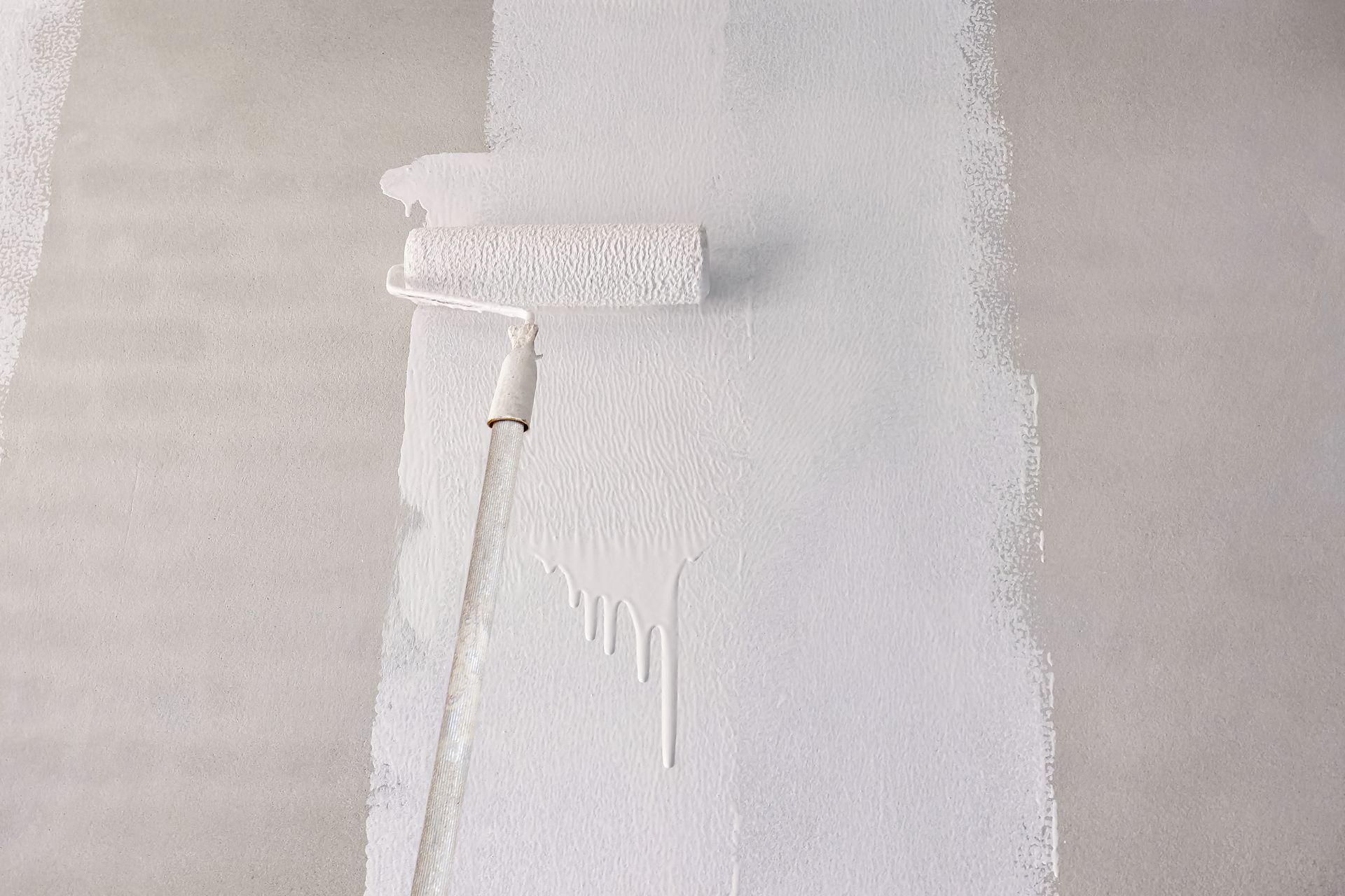 White paint roller on a wall, applying a coat of white paint.