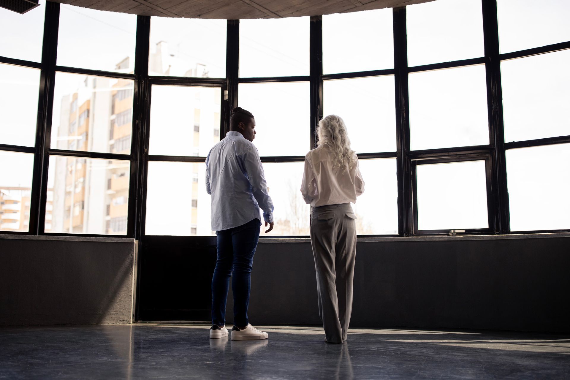 A man and a woman are standing in front of a large window.