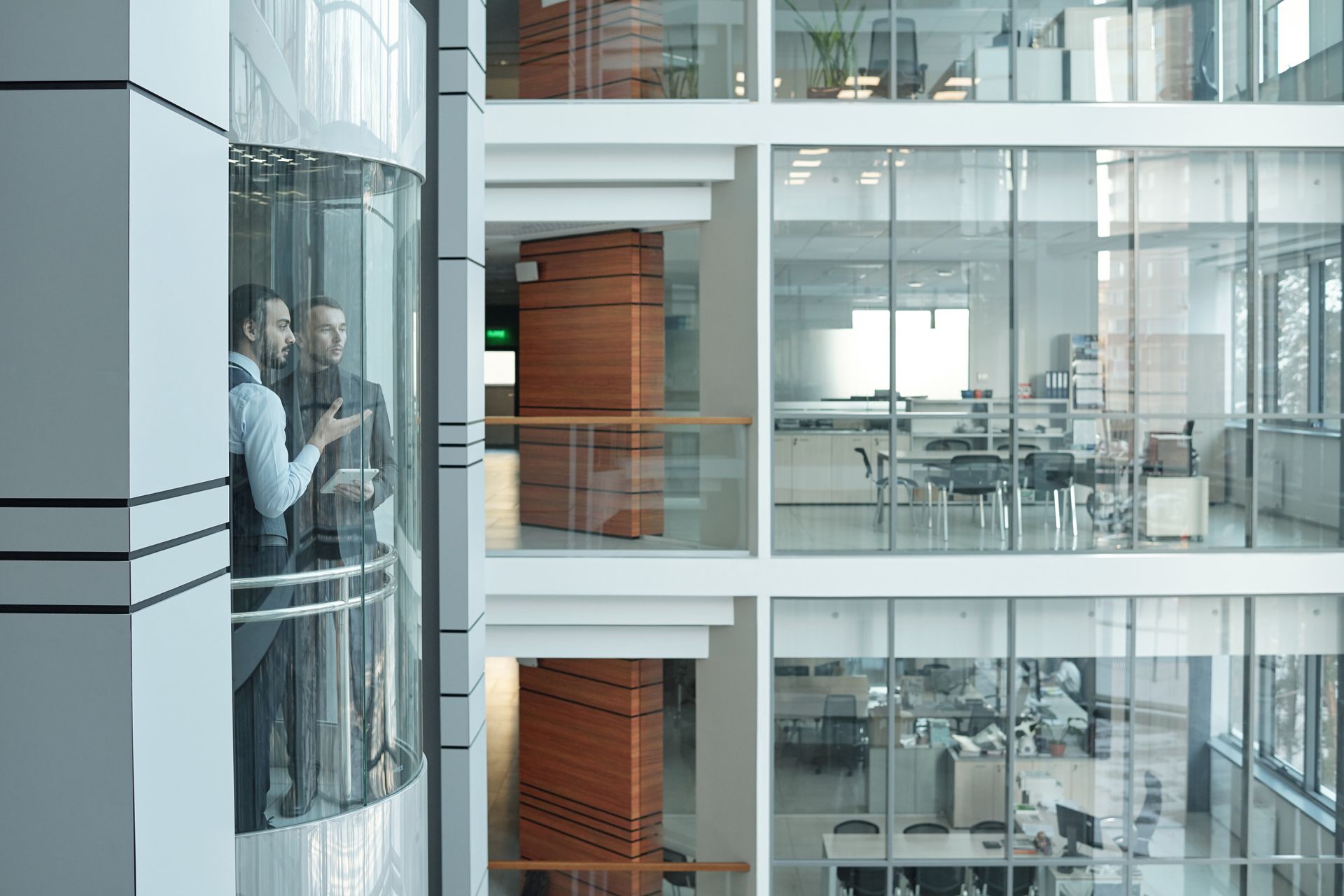 Two men are standing in an elevator in an office building.