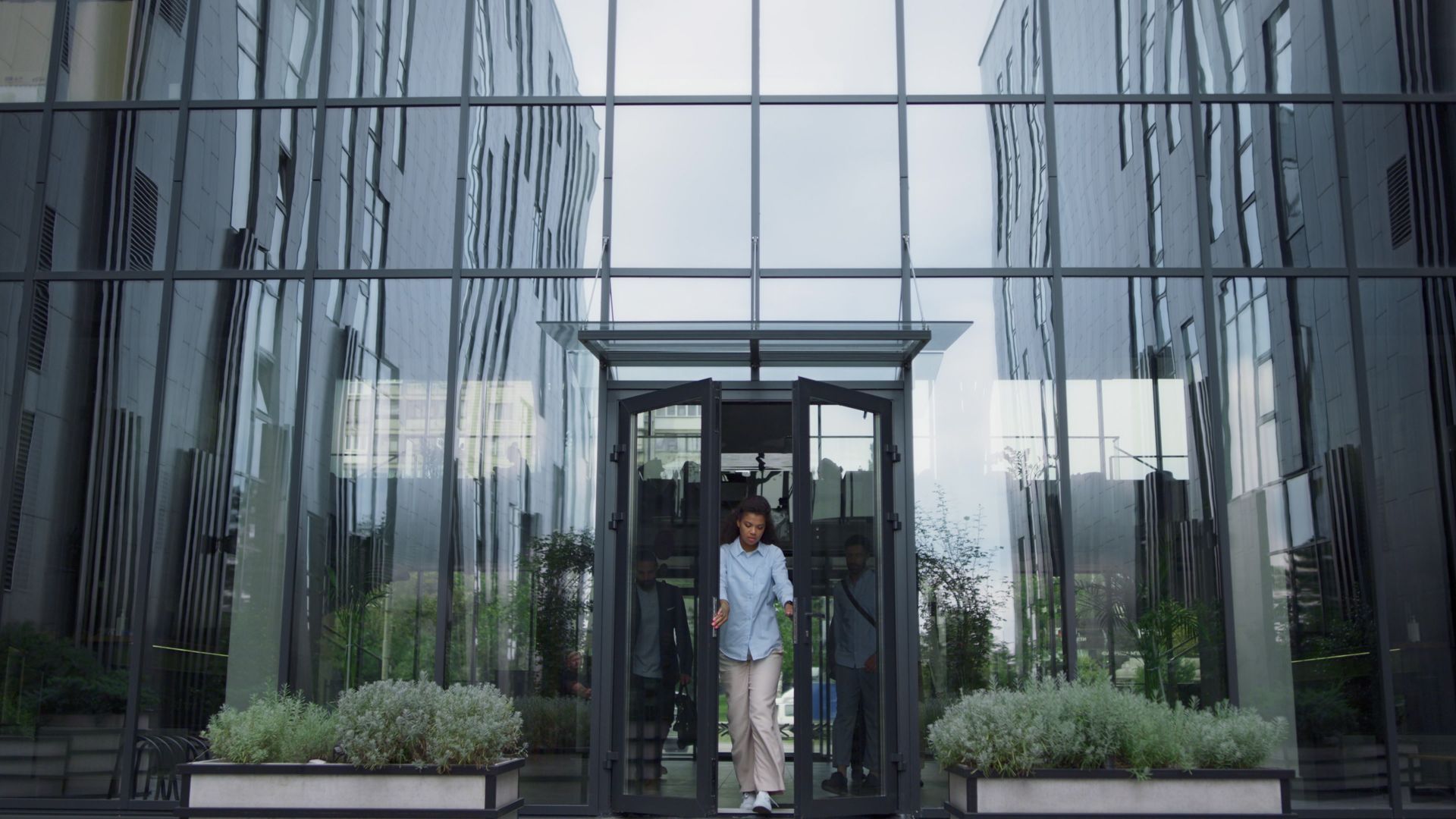 A man is talking on a cell phone while walking out of an office building.