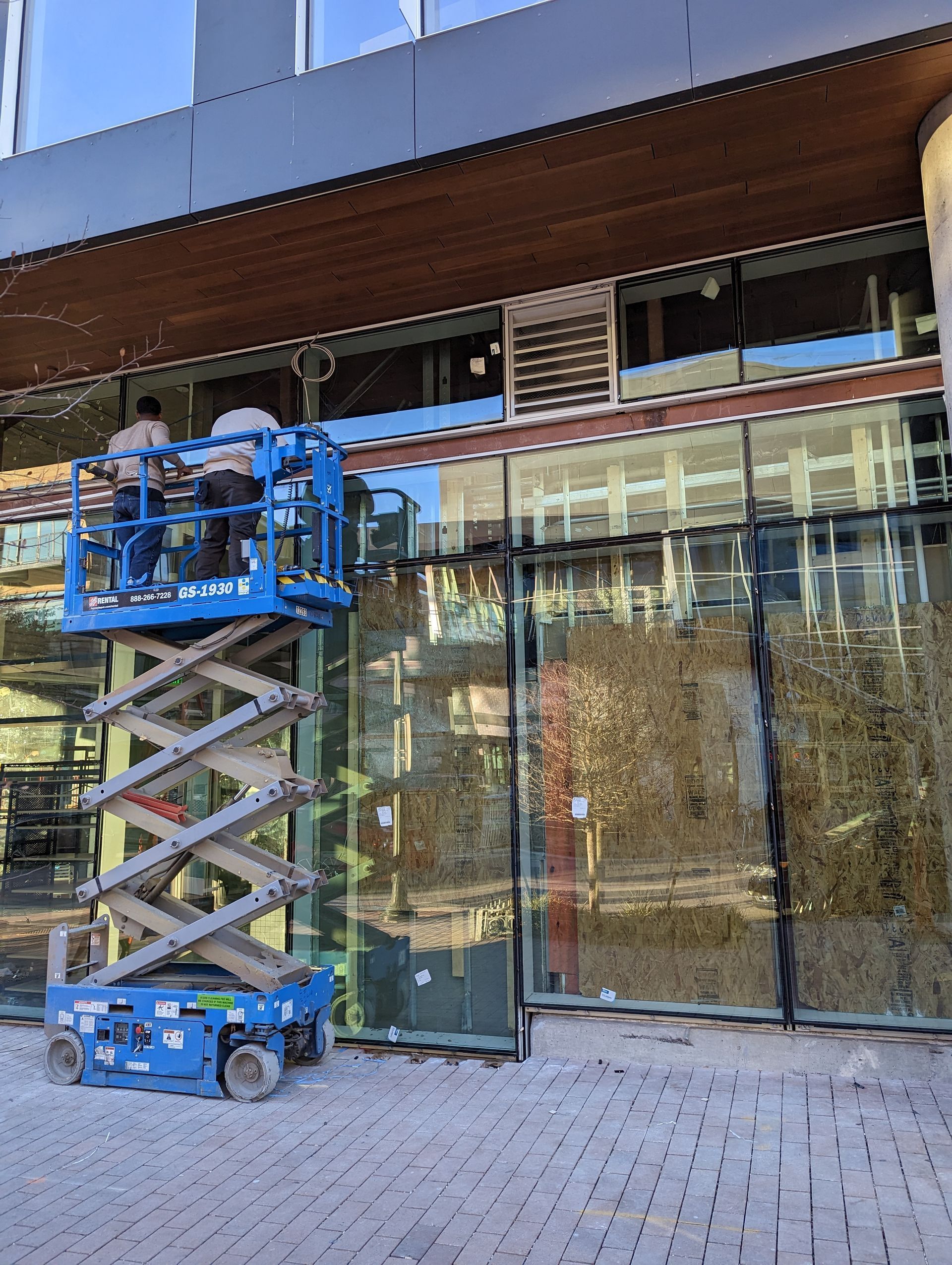 A man is standing on a scissor lift in front of a building.