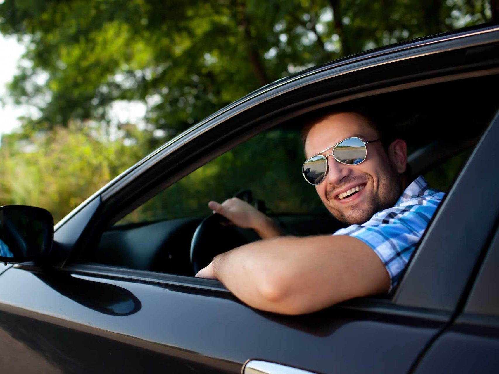 A man wearing sunglasses is smiling while driving a car