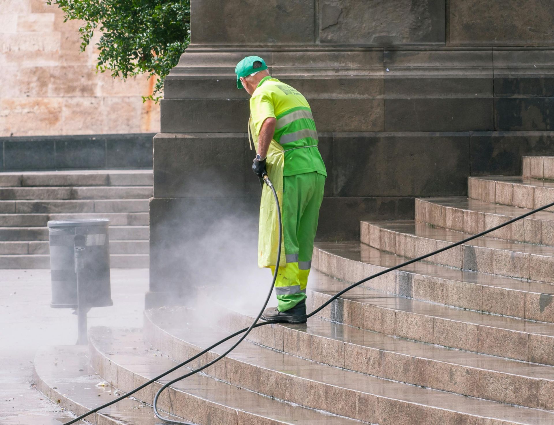 A person wearing bright orange rubber gloves is using a hose to clean the tile floor.