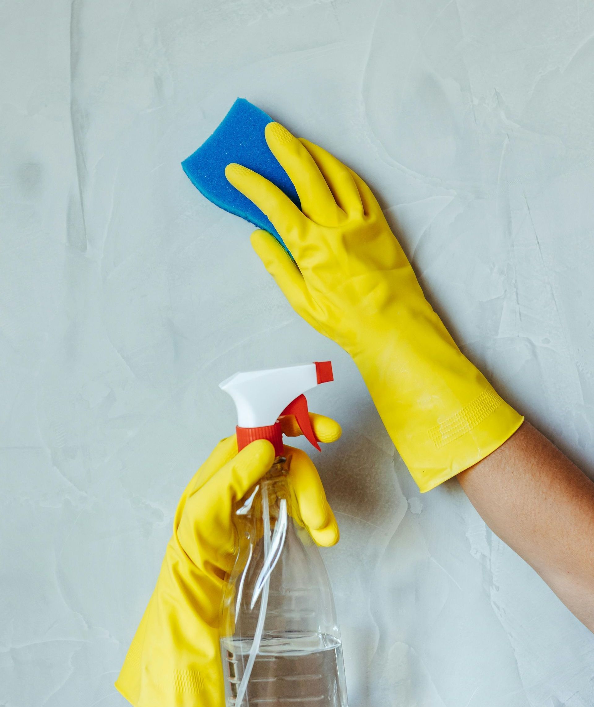 A person wearing bright orange rubber gloves is using a hose to clean the tile floor.