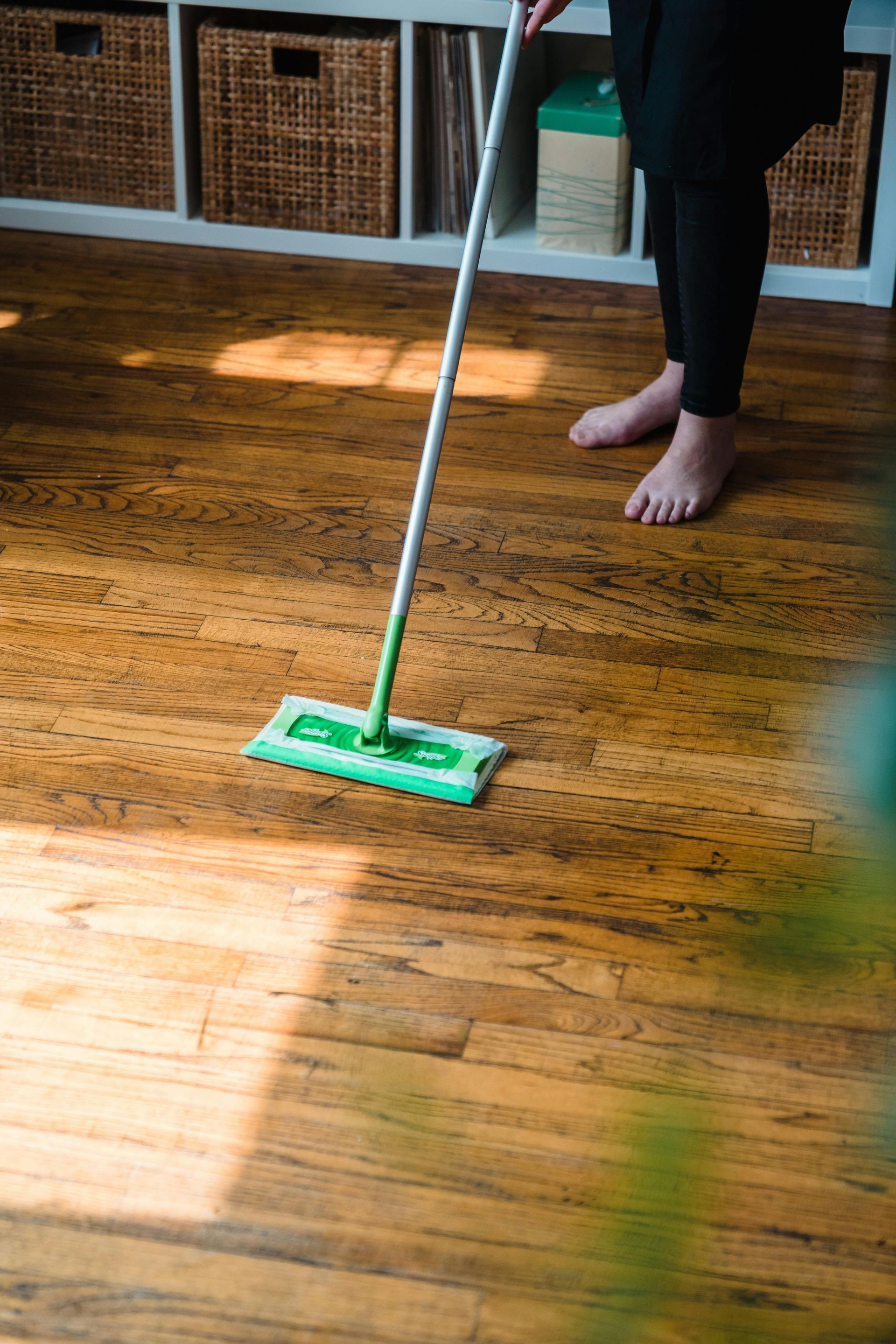 A person wearing bright orange rubber gloves is using a hose to clean the tile floor.