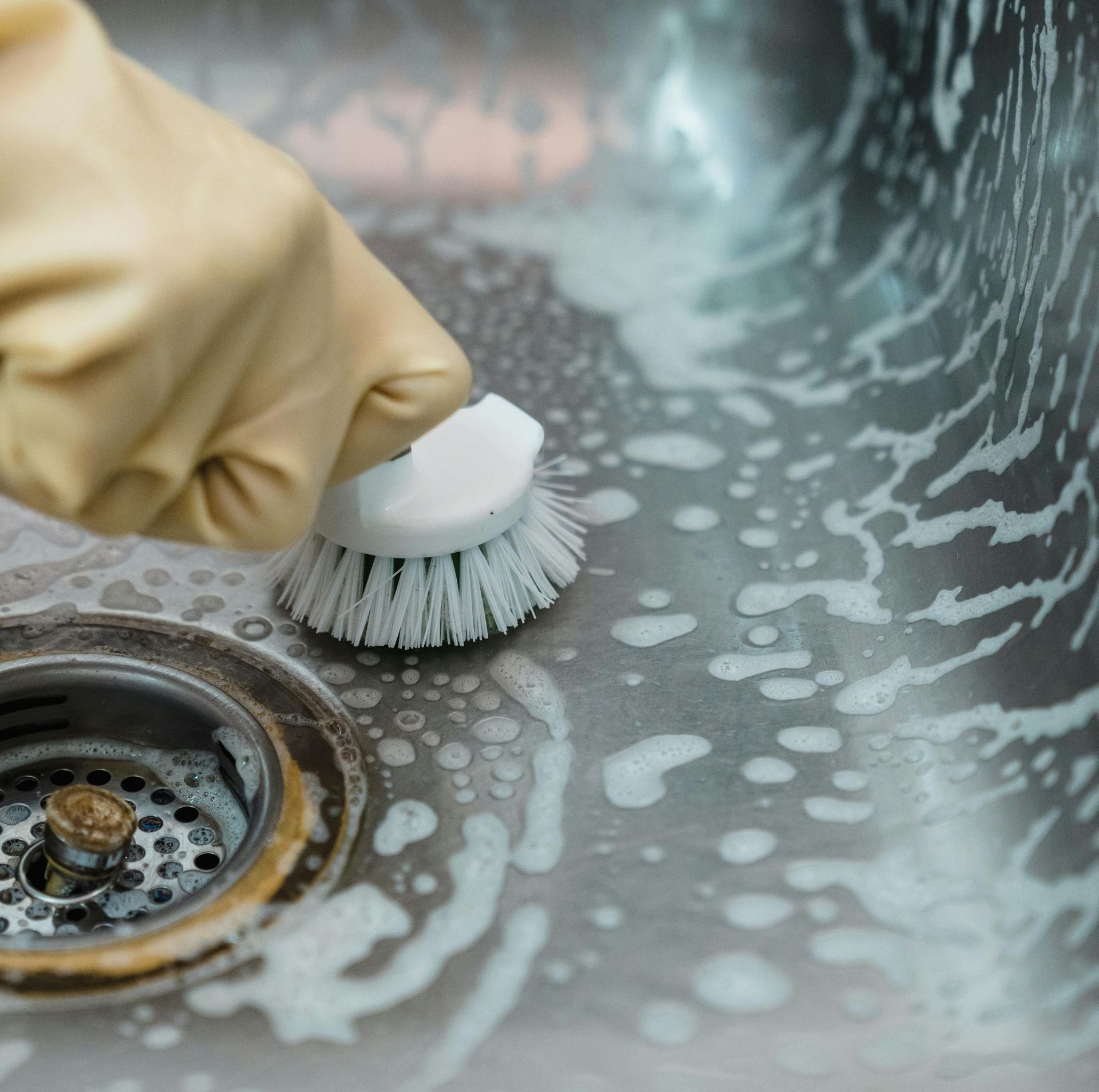 Professional cleaner meticulously scrubbing grout lines with a specialized brush and foamy soap on a sleek gray tiled bathroom floor.