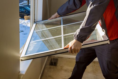 Person holding a window pane with white frame. Indoors, window opening visible. Winter scene outside.
