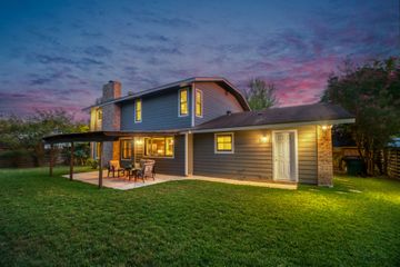 Backyard of a two-story blue house with patio and lush green lawn at dusk.