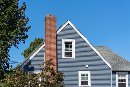 Brick chimney on a blue-sided house with white-framed windows against a clear blue sky.