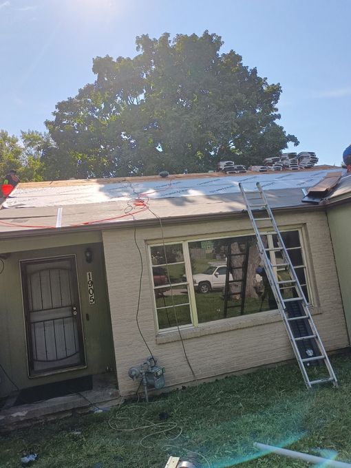A man is standing on a ladder on the roof of a house.