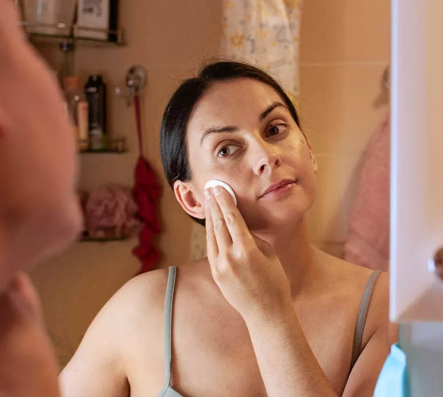 Botella de producto para el cuidado de la piel de color blanco, con banda y etiqueta plateadas, en posición vertical.