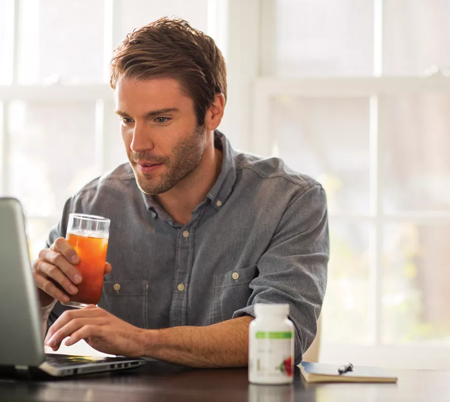 Hombre trabajando en una computadora portátil, bebiendo bebidas, con botella de suplemento.