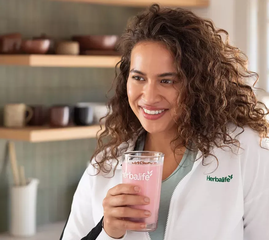 Caja de Herbalife Protein Crunch, sabor chocolate. Una cuchara vierte trozos crujientes en un batido.