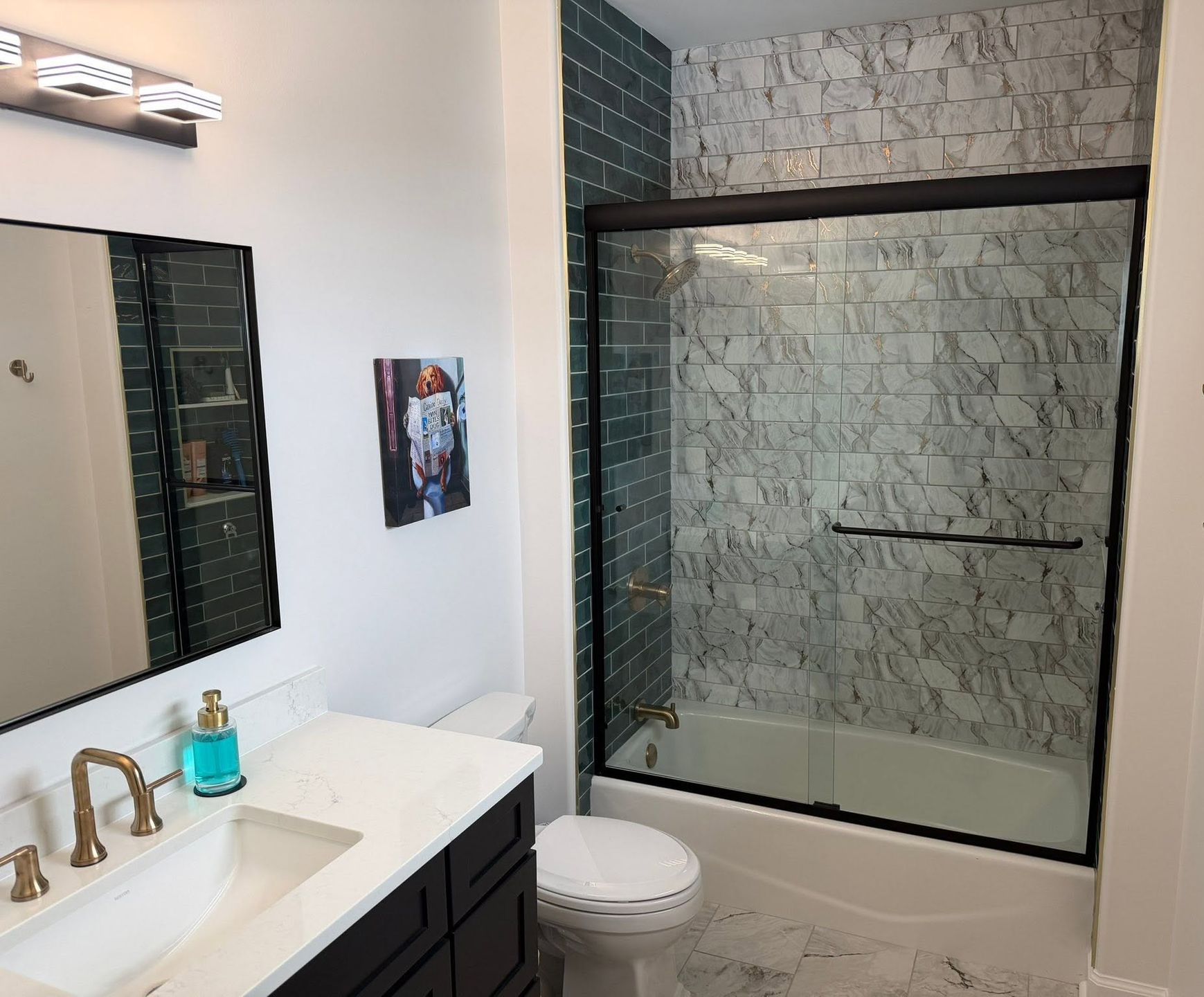 Modern bathroom with black vanity, white countertop, glass shower, and marble tile walls.