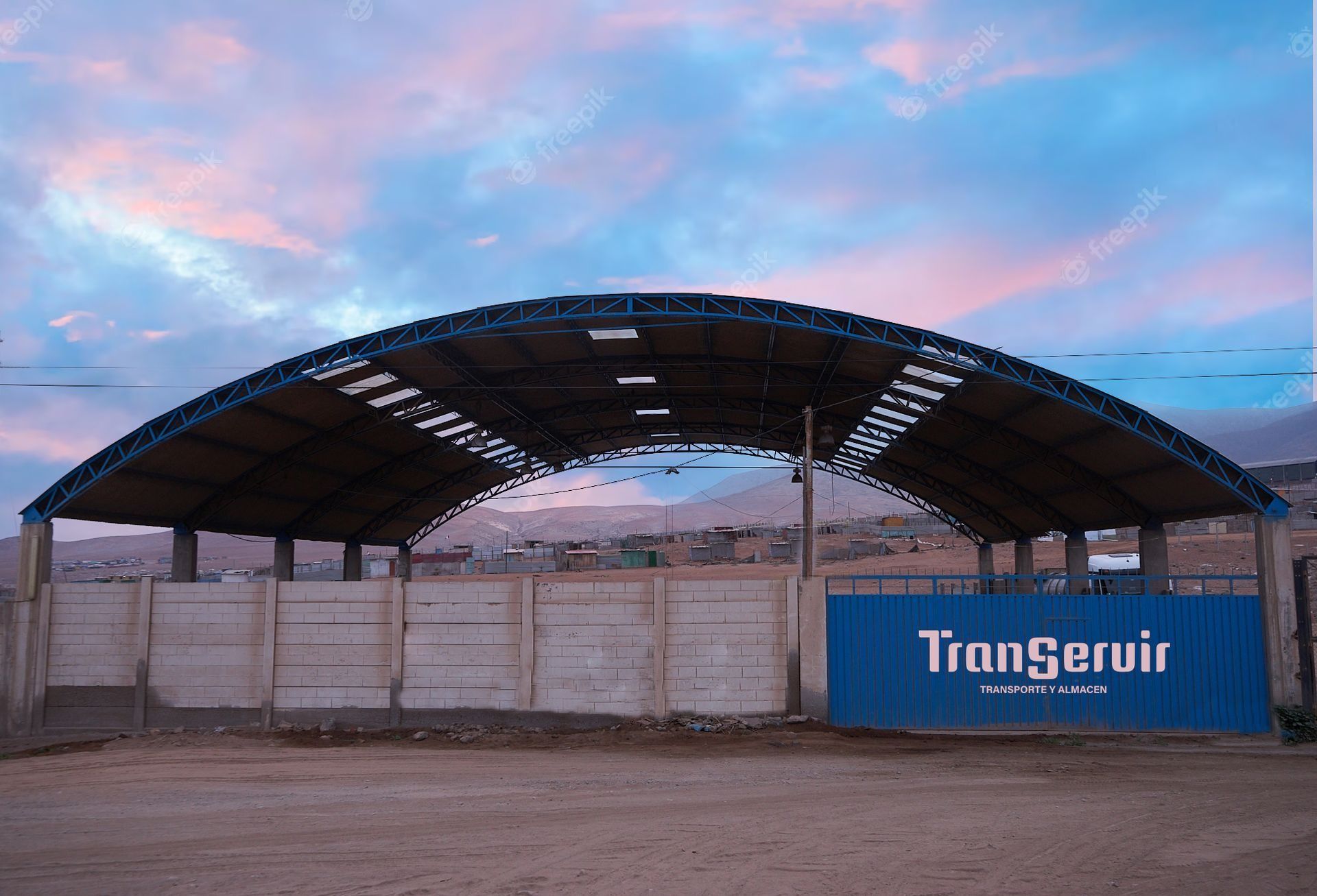 Almacén abierto con un contenedor azul “TimgenAir” bajo un techo curvo al anochecer.