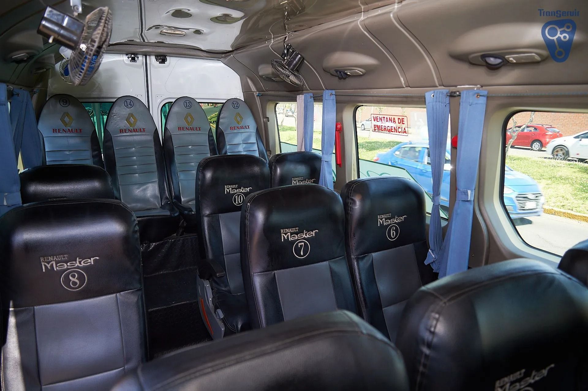 Asientos vacíos de cuero negro en el interior de un minibús con cortinas azules y ventanas abiertas.