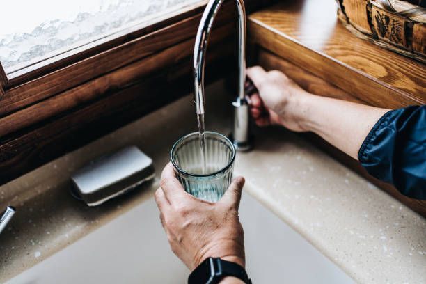 Man filling glass with filtered tap water at home sink, showcasing modern water treatment system.