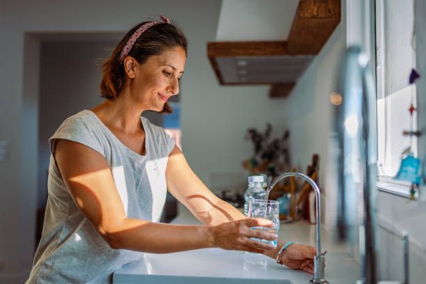 A beautiful woman fills a glass with filtered water directly from the tap.