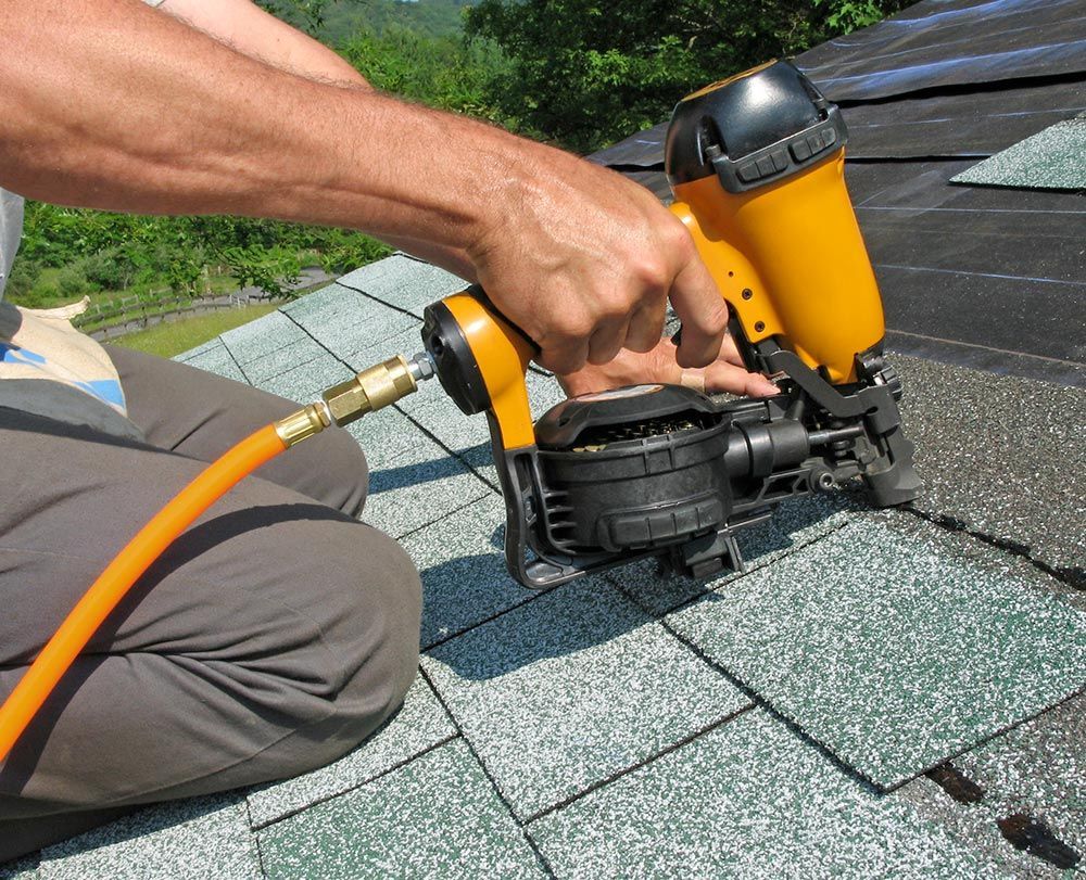 A man installs a shingled roof with a nail gun in Kettering, OH, showcasing Bauer Roofing Siding Win