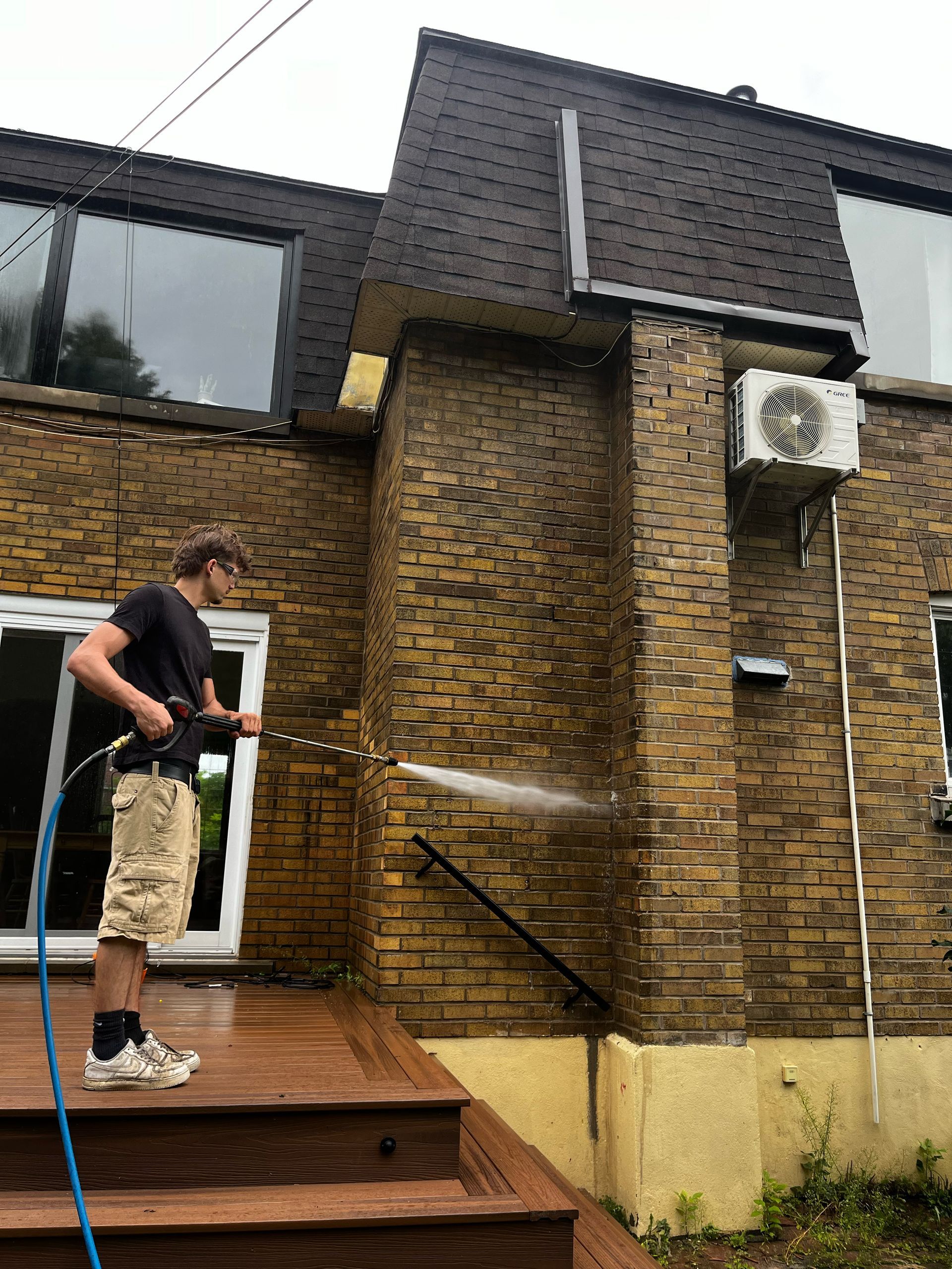A man is cleaning the side of a brick building with a hose.