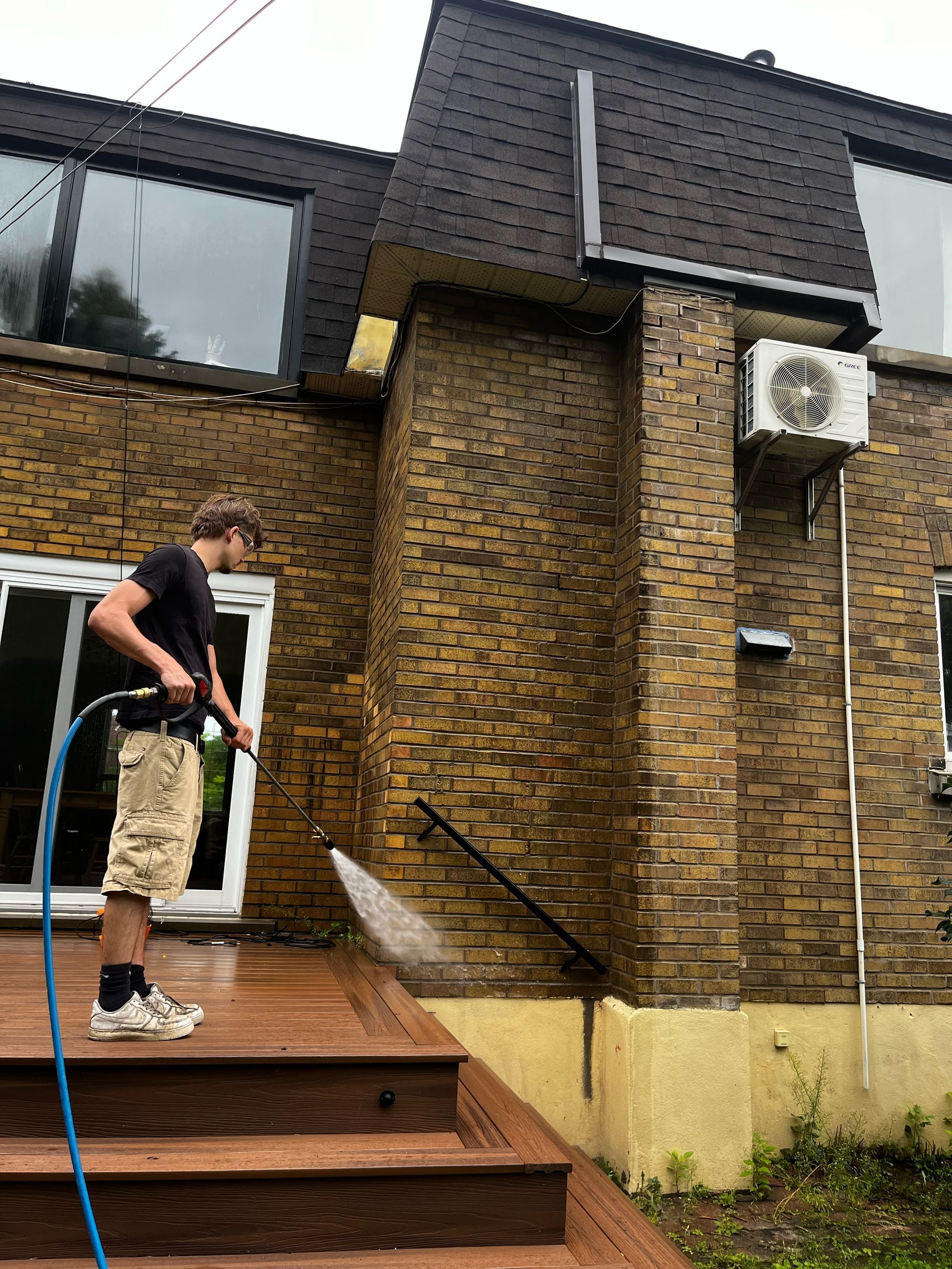 Un homme nettoie le côté d'un bâtiment en briques avec un nettoyeur haute pression.