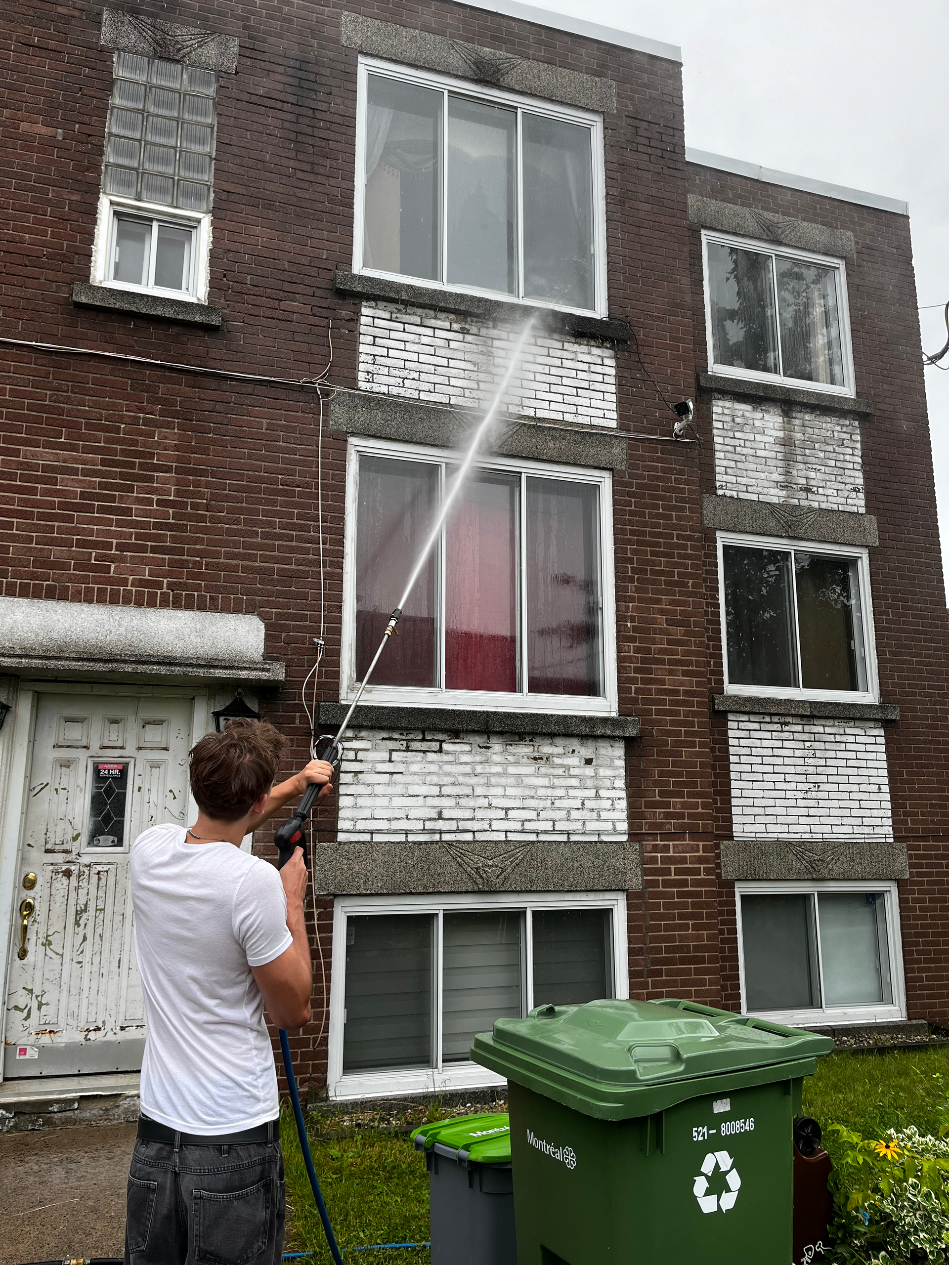 A man is cleaning a brick building with a high pressure washer.